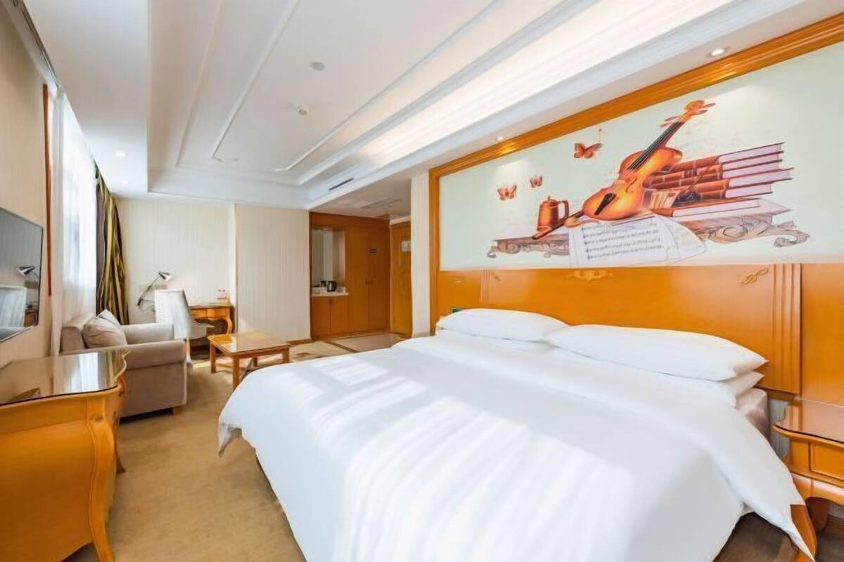 A hotel room with a large bed, a desk, a chair, and a wall mural.