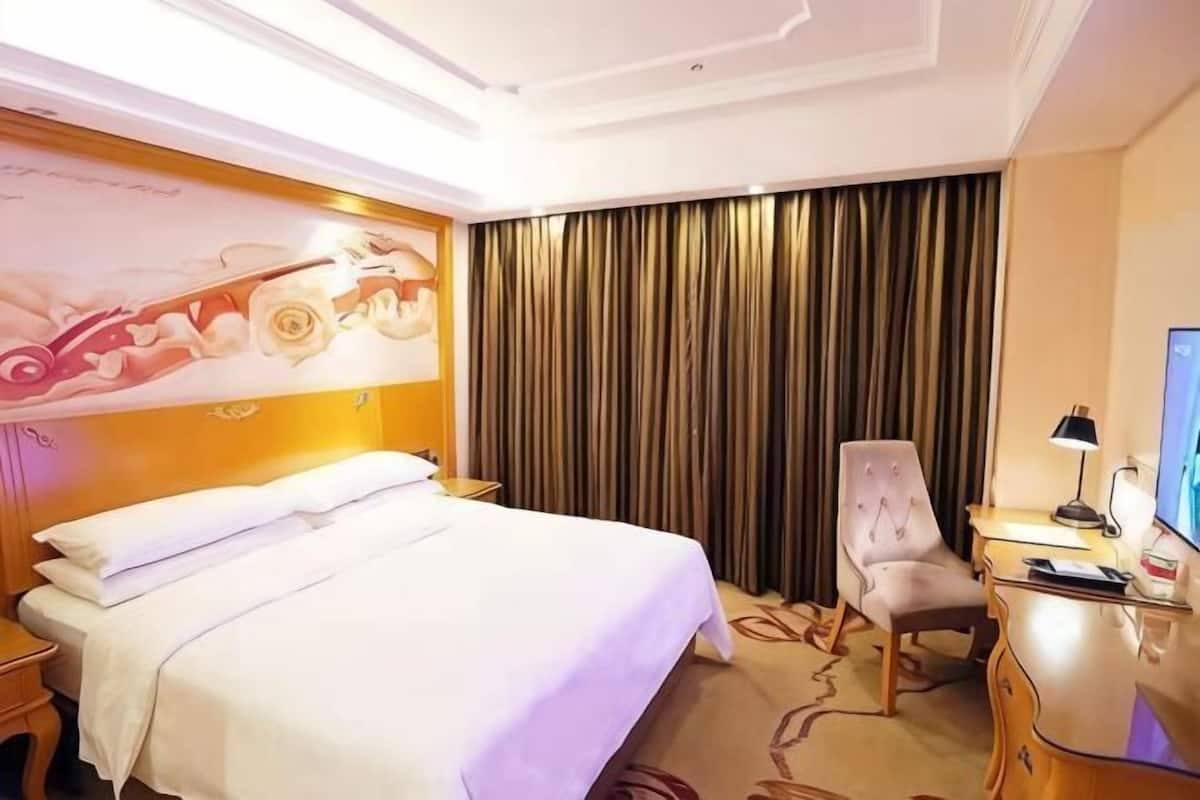 A hotel room with a bed, a desk, a chair, a television, and a curtain.