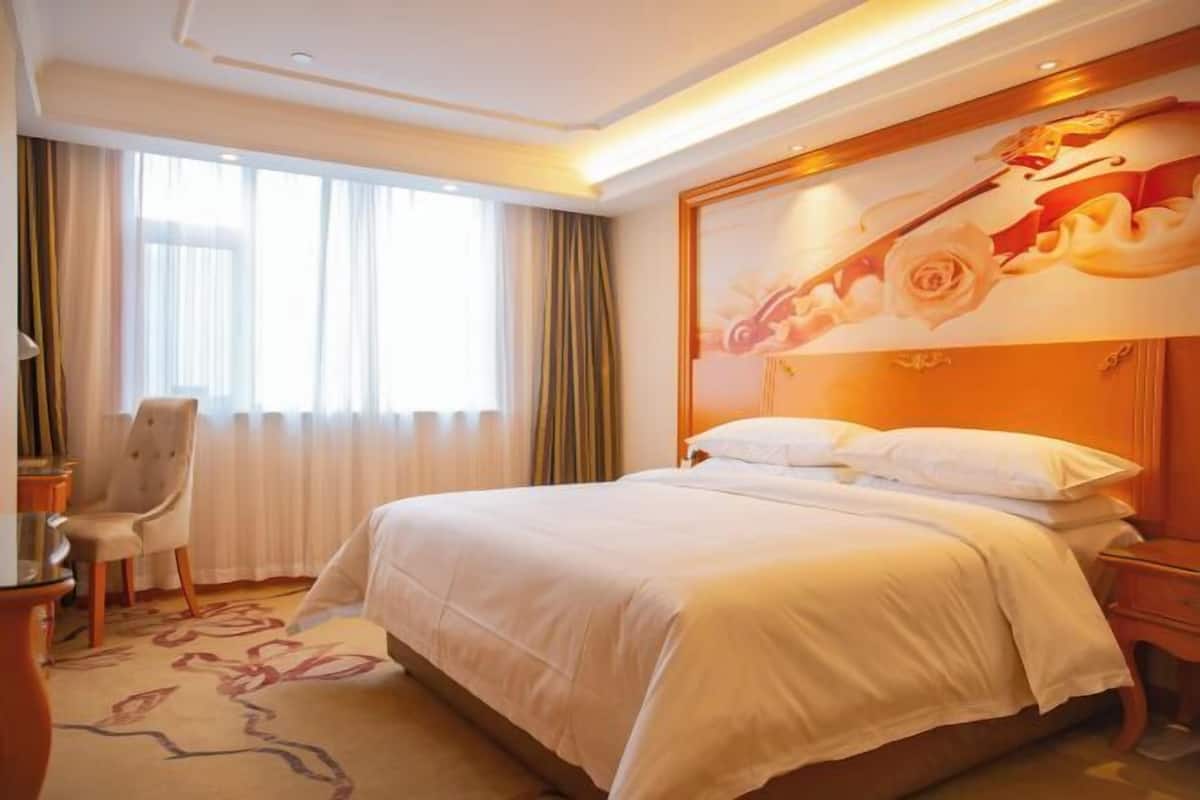 A hotel room with a large bed, a desk, and a chair.