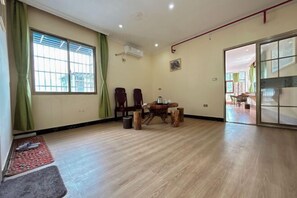 Una habitación amplia con suelo de madera, una mesa de comedor con sillas, un gran ventanal con cortinas y un cerramiento de vidrio corredera que da a otra habitación.