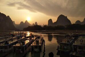 A riverfront with boats docked, a bridge, and mountains in the background. - Shengjin Hotel (Yangshuo)