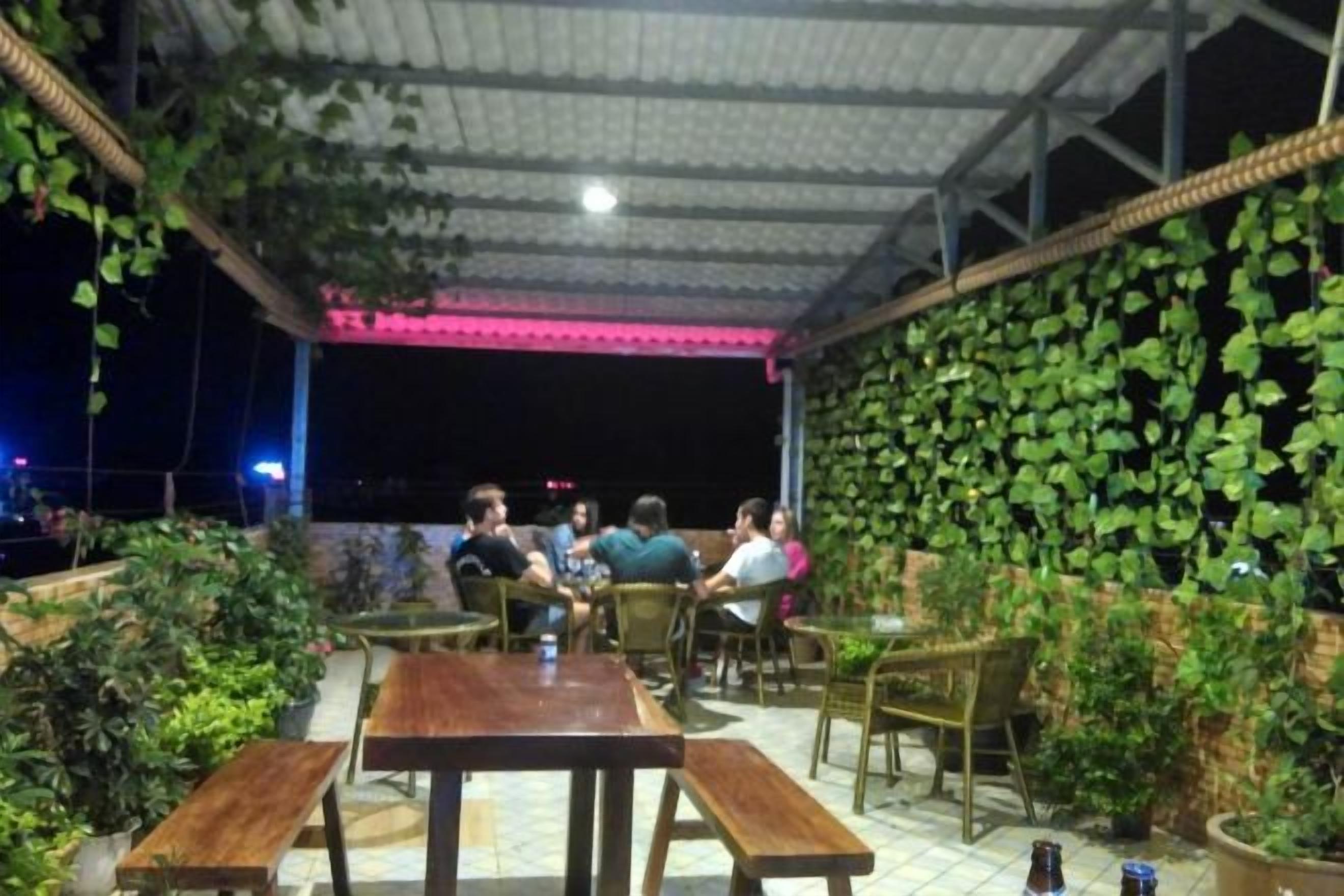 An outdoor seating area with tables and chairs, surrounded by greenery and a tiled floor.
