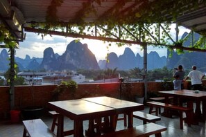 An outdoor dining area with tables and benches, overlooking a mountainous landscape. - Shengjin Hotel (Yangshuo)