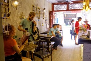 A cafe with tables and chairs, a person standing with a phone, and another person sitting. - Shengjin Hotel (Yangshuo)