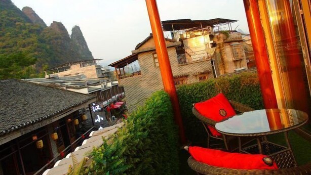 A traditional building with a tiled roof, a balcony with wicker furniture, and a view of a mountainous landscape. - Shengjin Hotel (Yangshuo)