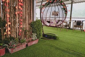 A hanging chair with a decorative net, a bamboo wall with plants, and a grassy area. - Shengjin Hotel (Yangshuo)