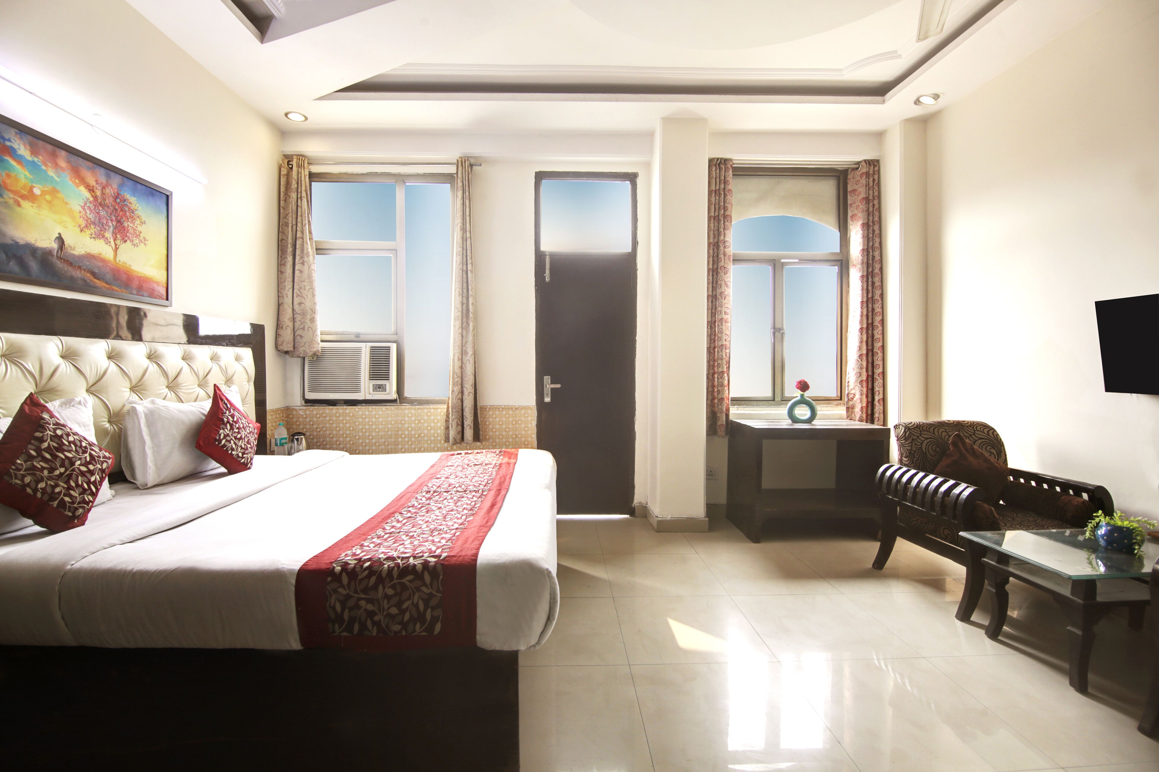 A hotel room with a large bed, a sofa, a small table, a TV, and a window with curtains.