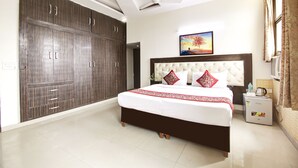 A bedroom with a large bed, a wardrobe, a painting on the wall, and a small table with a kettle. - Hotel Vibe Blue (Noida)