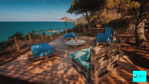 A wooden deck with outdoor seating, overlooking a coastal area with a clear view of the sea and a distant island. - Villa Ortensia (Mazzaforno)