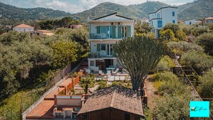 A two-story house with a balcony, surrounded by greenery and hills. - Villa Ortensia (Mazzaforno)
