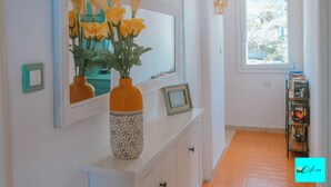 A hallway with a white cabinet, a mirror reflecting yellow roses, and a window with a view of trees. - Villa Ortensia (Mazzaforno)
