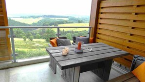 Un balcón con una mesa y sillas de madera, un candelabro de cristal y vistas a un paisaje verde.
