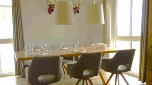 Comedor con una larga mesa dispuesta para cuatro personas, rodeada de sillas modernas con patas de madera.