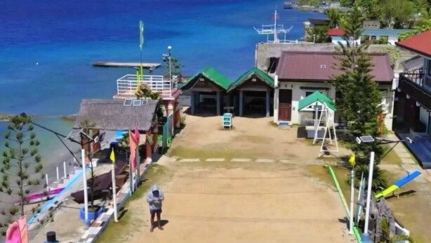 A beachside view with a sandy area, a small building, and a clear blue sky. - RGV Beach resort (Calatagan)