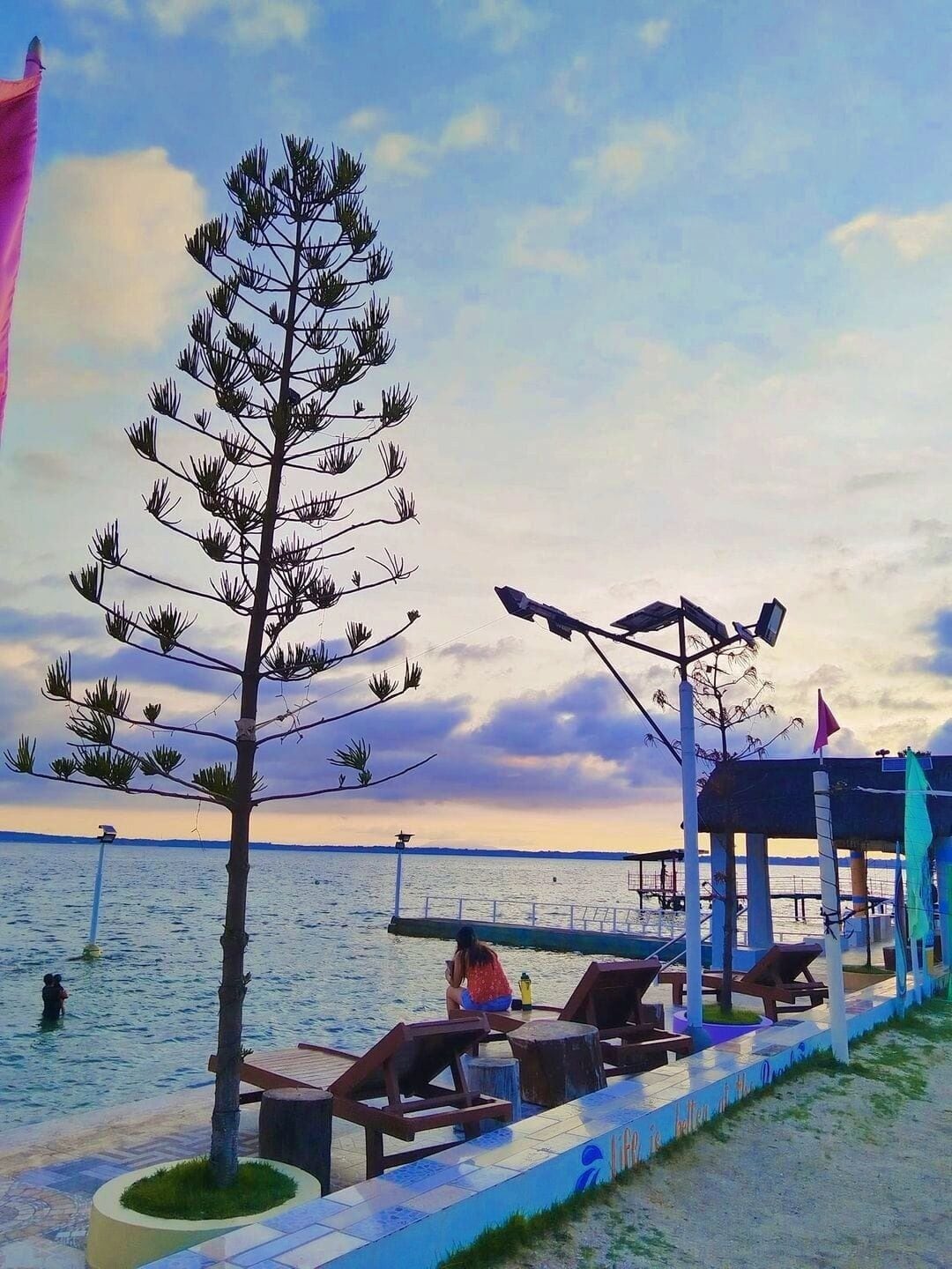 A beachside area with lounge chairs, a gazebo, and a large tree.