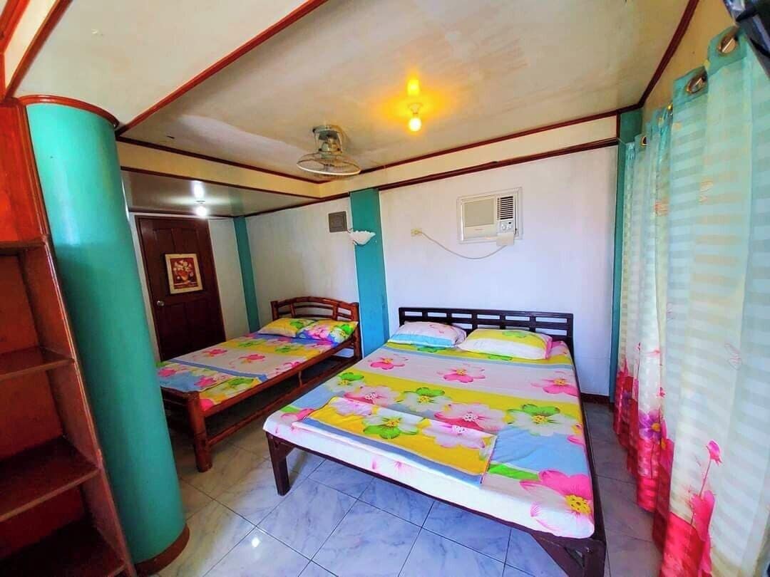 A room with two single beds, a ceiling fan, a wall-mounted air conditioner, and a window with curtains.