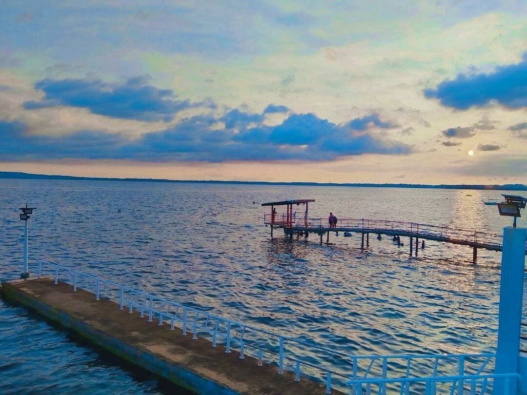 Eine Mole, die sich in ruhiges Wasser erstreckt, mit wolkenlosem Himmel darüber.