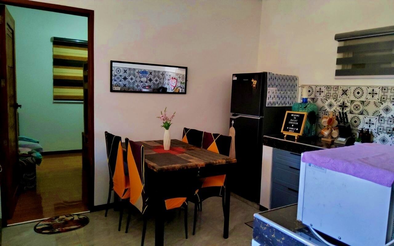 Una cocina compacta con refrigerador, una mesa de comedor con sillas naranjas y un pequeño rincón de comedor.