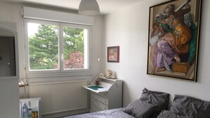 A bedroom with a bed, a window, a radiator, a desk, and a painting. - Juste une Chambre Chez L'habitant (Saint-Sébastien-sur-Loire)
