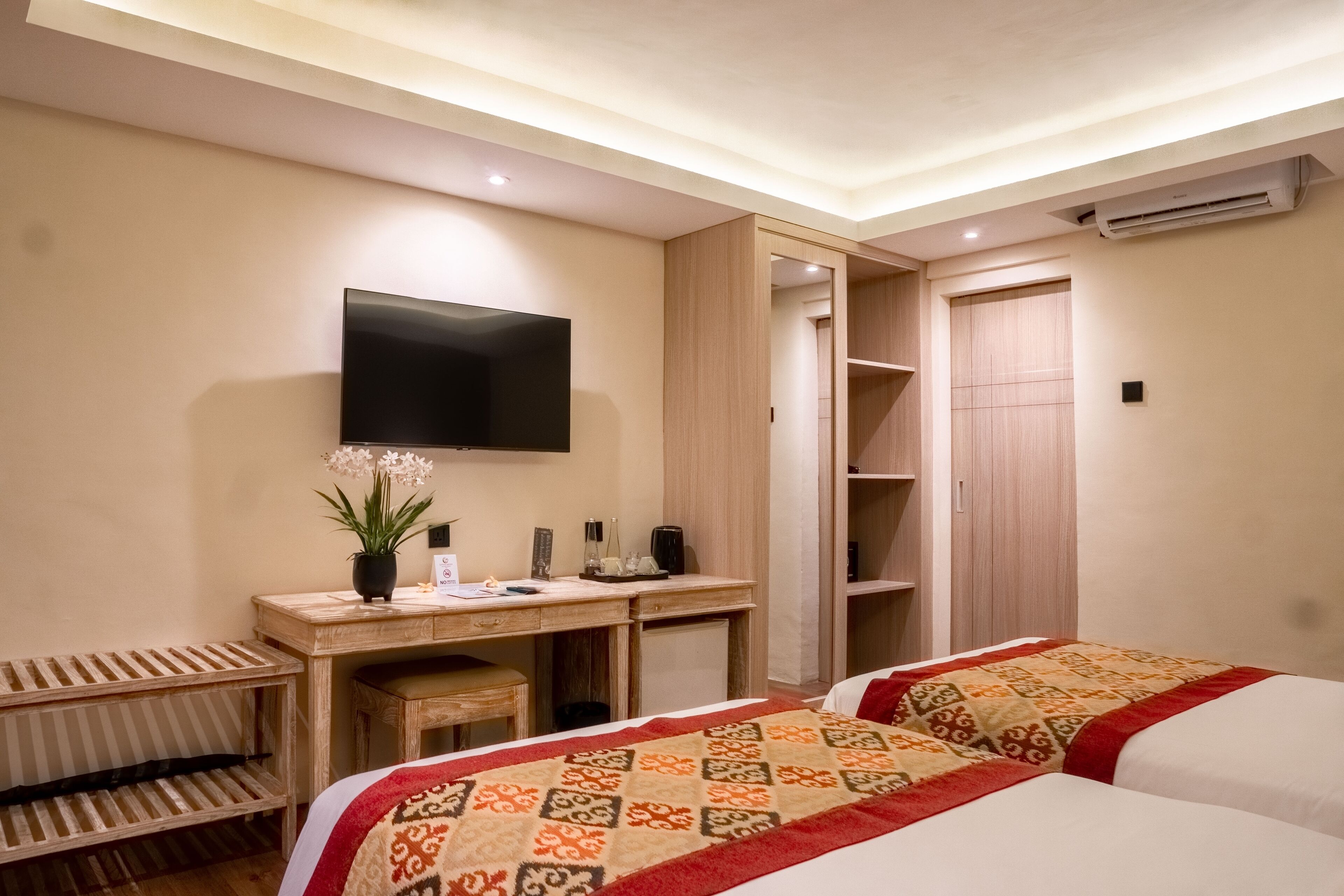 A hotel room with a bed, a desk with a flat-screen TV, a wardrobe, and a small seating area.