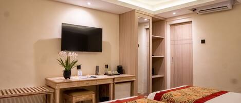 A hotel room with a bed, a desk with a flat-screen TV, a wardrobe, and a small seating area.