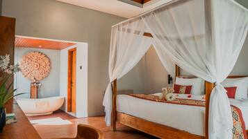 A bedroom with a wooden bed, white bedding, a canopy, a decorative wall piece, and a wooden side table with a bowl.