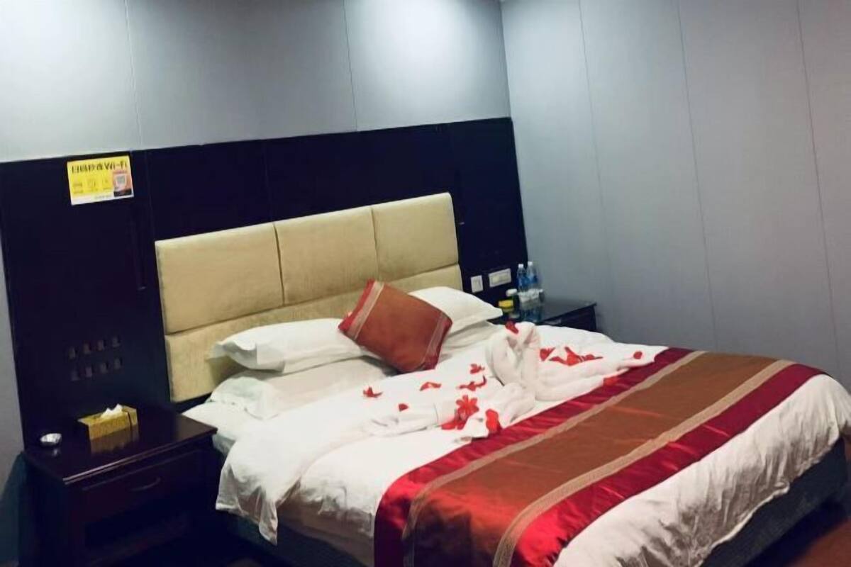 Une chambre d’hôtel avec un lit, une table de chevet, une étagère fixée au mur et un panneau sur le mur.