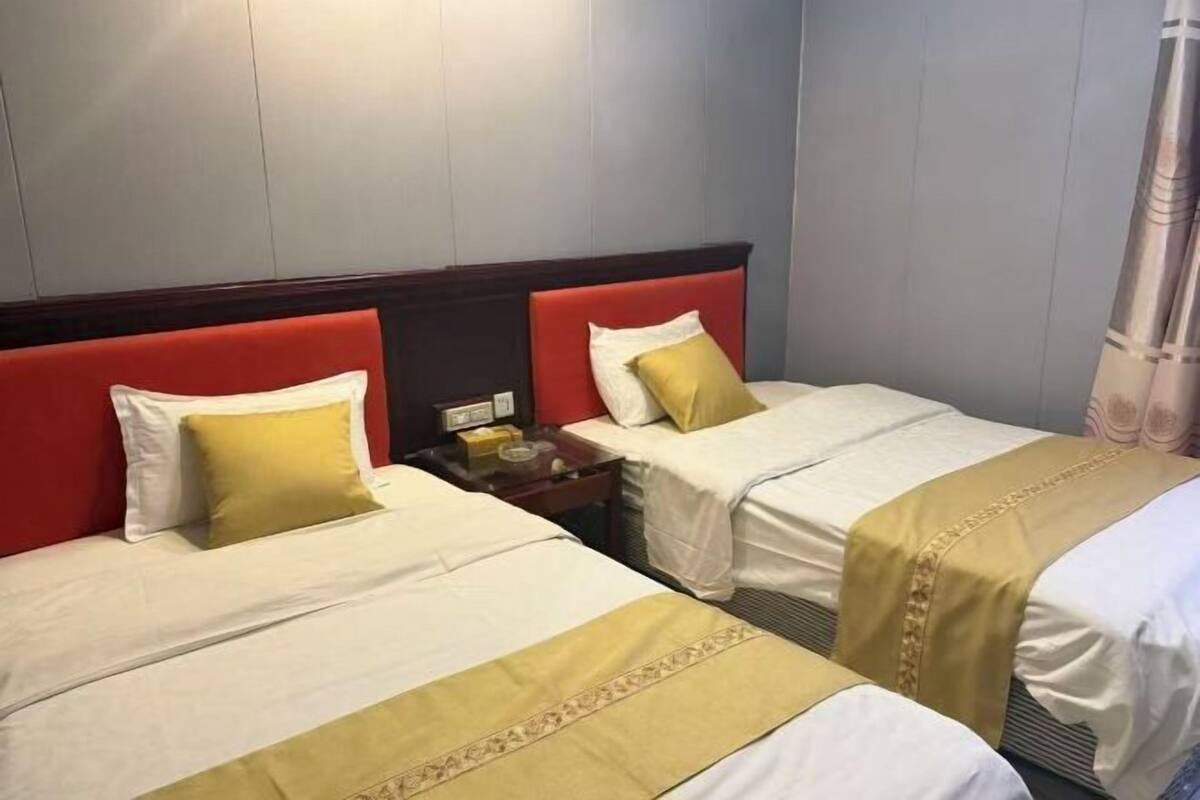 Une chambre d’hôtel avec deux lits, chacun doté d’une tête de lit rouge, de draps blancs et d’un coussin jaune.