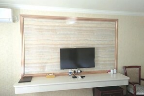 Una habitación con una televisión de pantalla plana grande montada en la pared, un escritorio blanco con una computadora portátil y una silla.