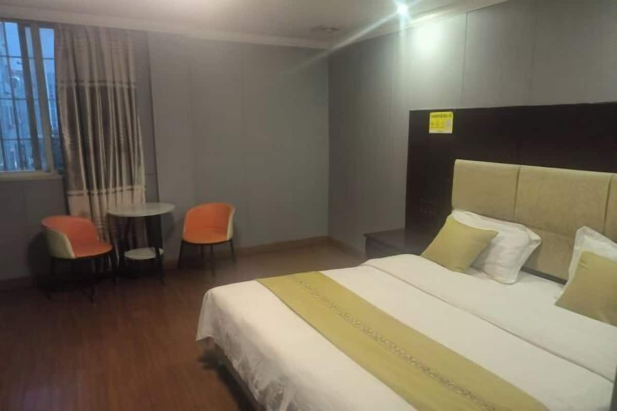 Une chambre d’hôtel avec un lit, deux chaises, une petite table et une fenêtre avec des rideaux.