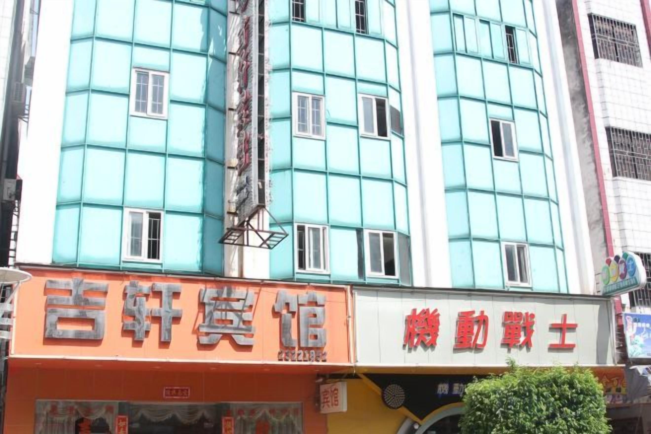 A building with a teal facade and multiple windows. There are signs for a hotel and a restaurant on the ground floor.