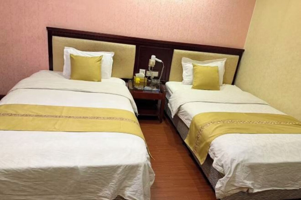 A hotel room with two beds, each with a headboard, a nightstand with a lamp, and a small table with a bottle and a glass.