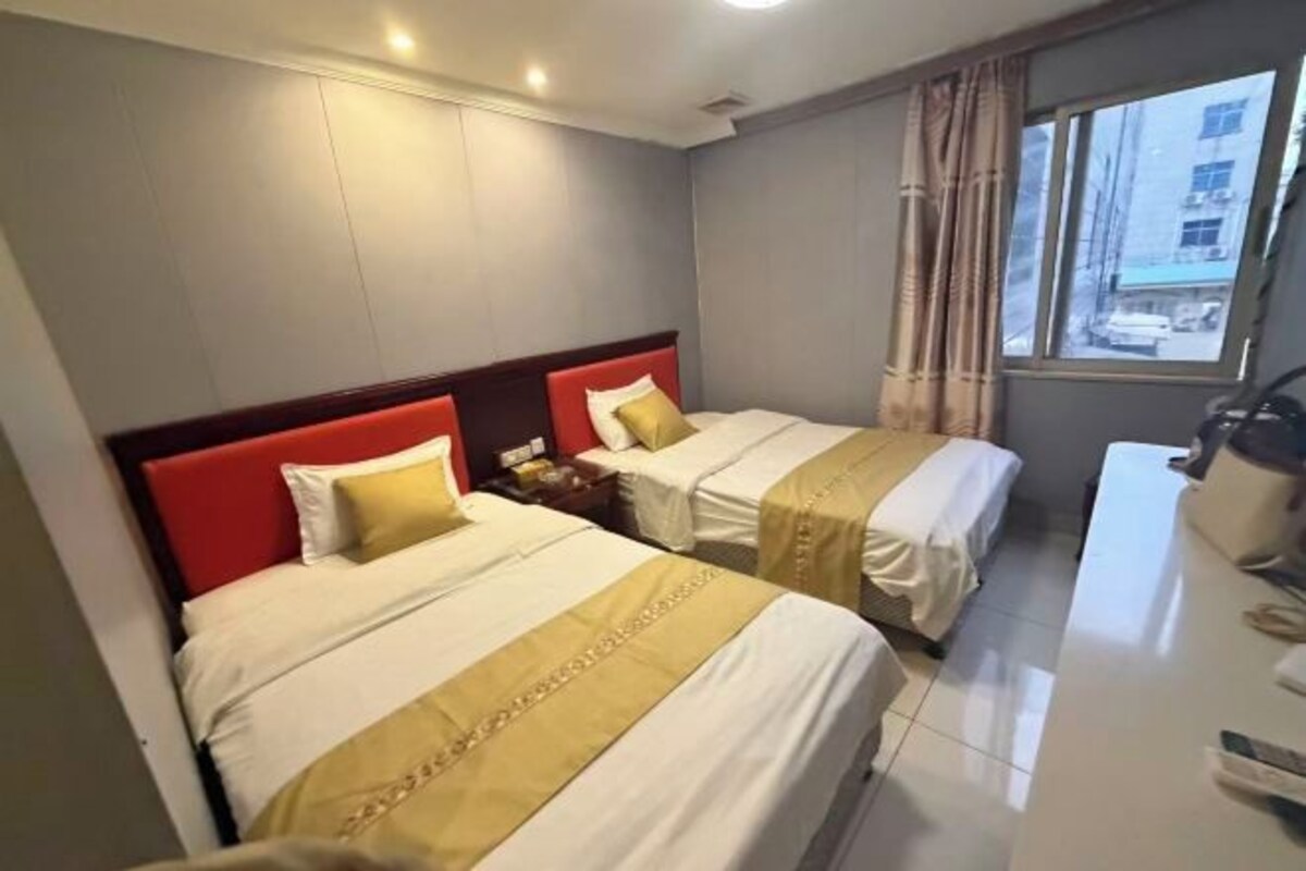 A hotel room with two beds, a desk, and a window.