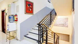 Un escalier avec des rampes noires, un distributeur d’eau et un extincteur, le tout situé à gauche.