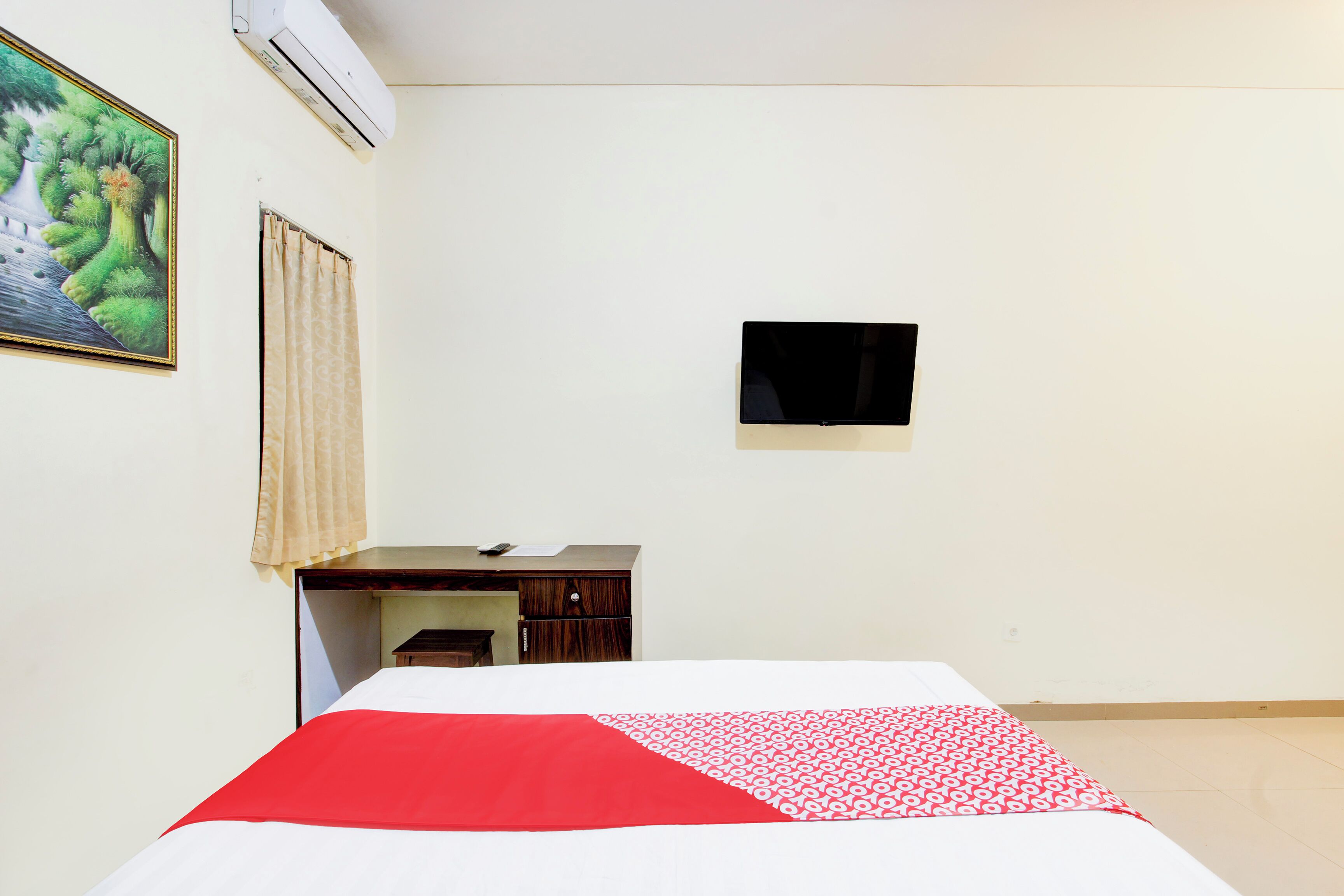 A hotel room with a bed, a desk, a chair, a TV, and a painting on the wall.