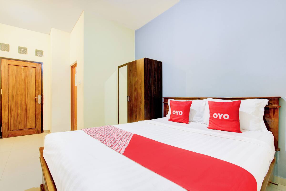 A hotel room with a bed, two pillows with the word "OYO" on them, a wooden wardrobe, and a mirror on the wall.