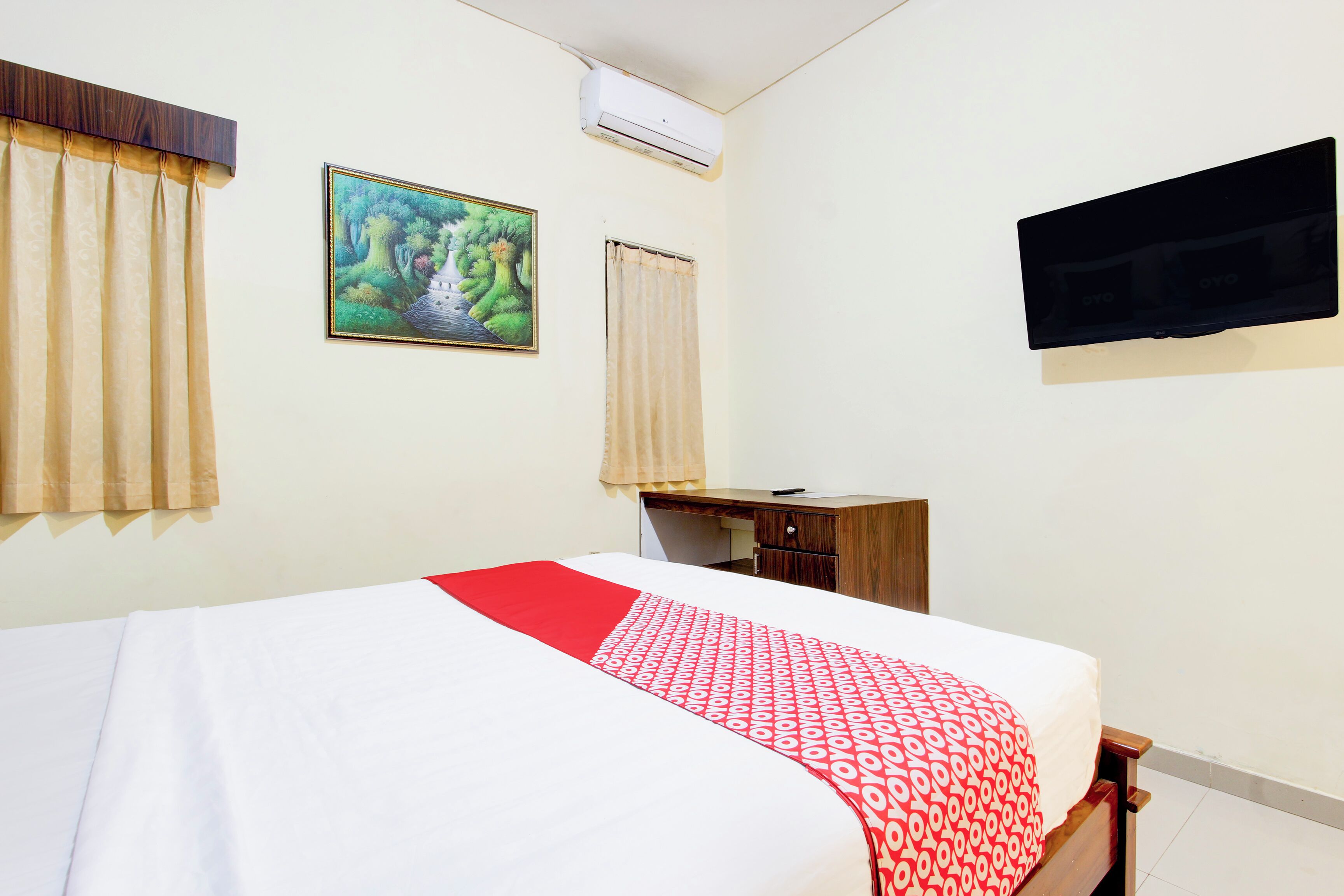 A hotel room with a bed, a desk, a chair, a TV, and a painting on the wall.