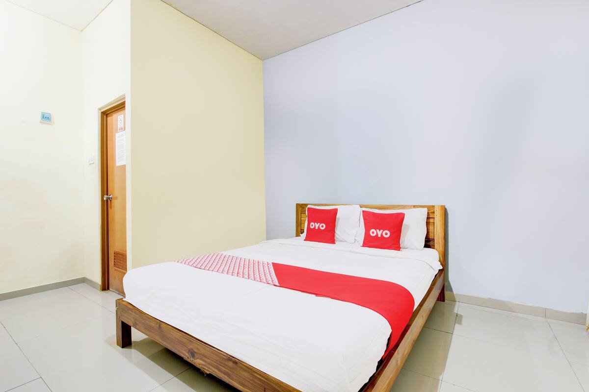 A neatly made bed with a wooden frame and white bedding, two red pillows with "OYO" text, and a red blanket.