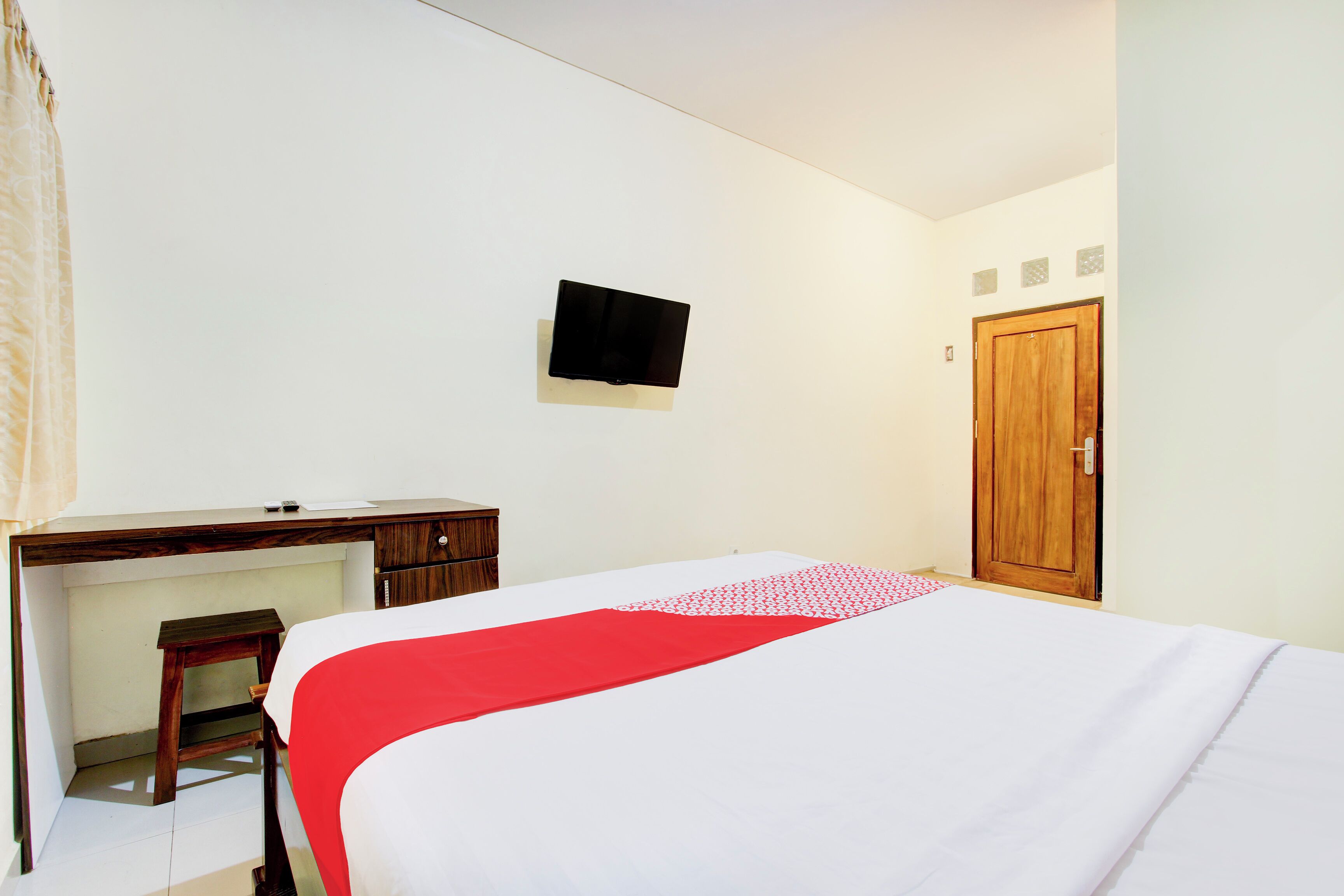 Ein Hotelzimmer mit Bett, Schreibtisch, Stuhl, Wandfernseher und Holztür.