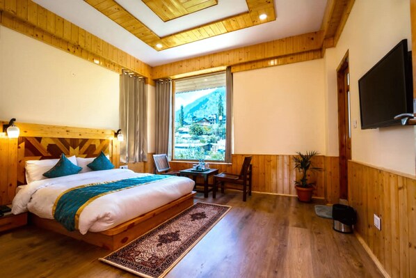 Un dormitorio con paneles de madera, una cama, un escritorio, una silla, un televisor y una ventana con vistas a la montaña.