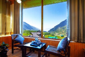 Una habitación de madera con un ventanal que da a un paisaje montañoso. Hay una mesa con sillas y una bandeja con botellas y vasos.
