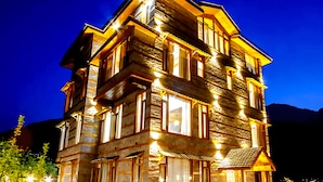 A multi-story building with a stone facade, multiple windows, and a small outdoor seating area. - Amber Cottage Manali (Manali)