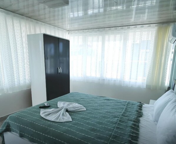 Ein Hotelzimmer mit Bett, Schrank und Fenster mit durchsichtigen Vorhängen.