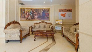 A lobby with three ornate sofas, a wooden coffee table, and a large classical painting on the wall. - Vienna Hotel (Dunhuang)