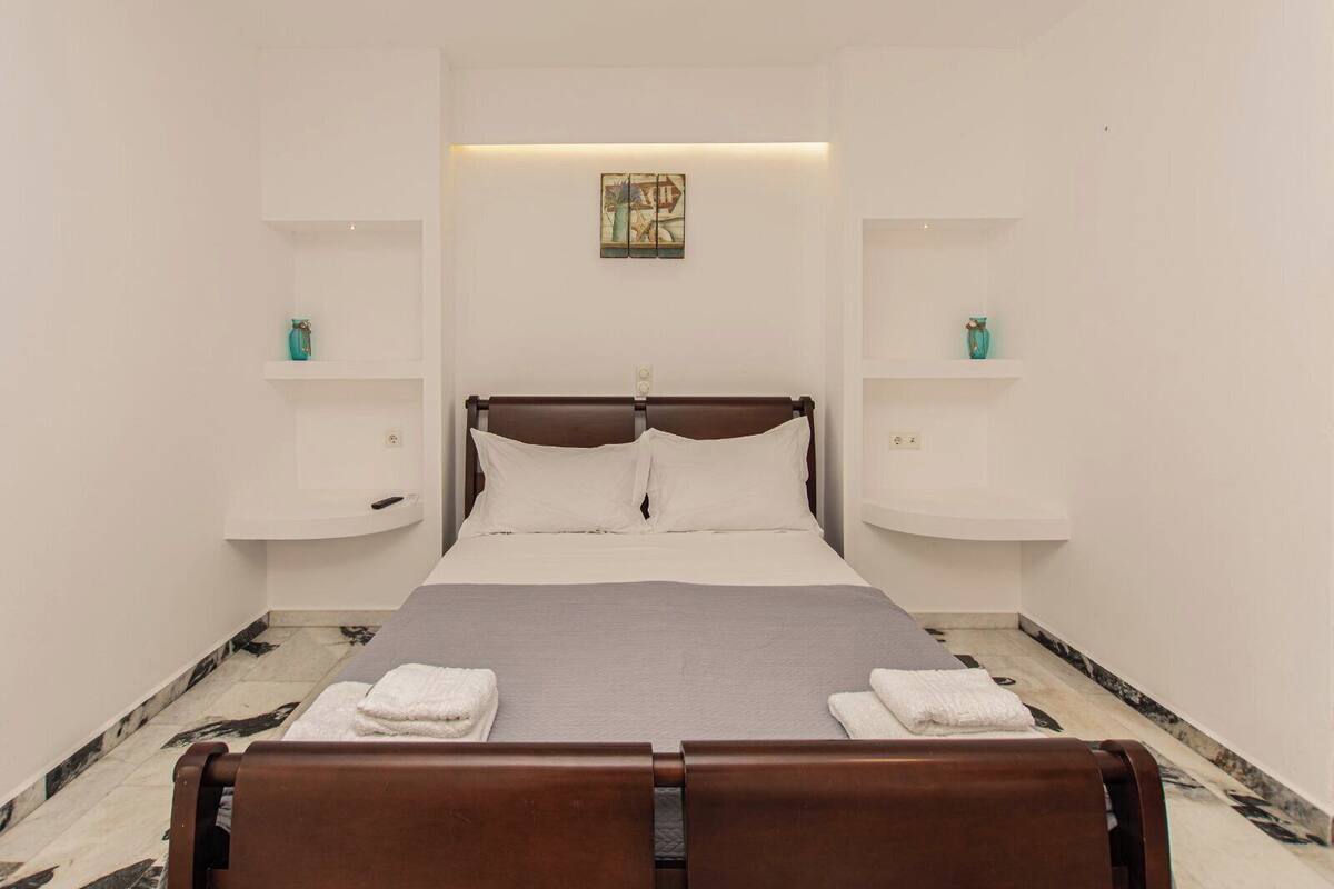 A hotel room with a bed, white walls, a marble floor, and a painting above the bed.