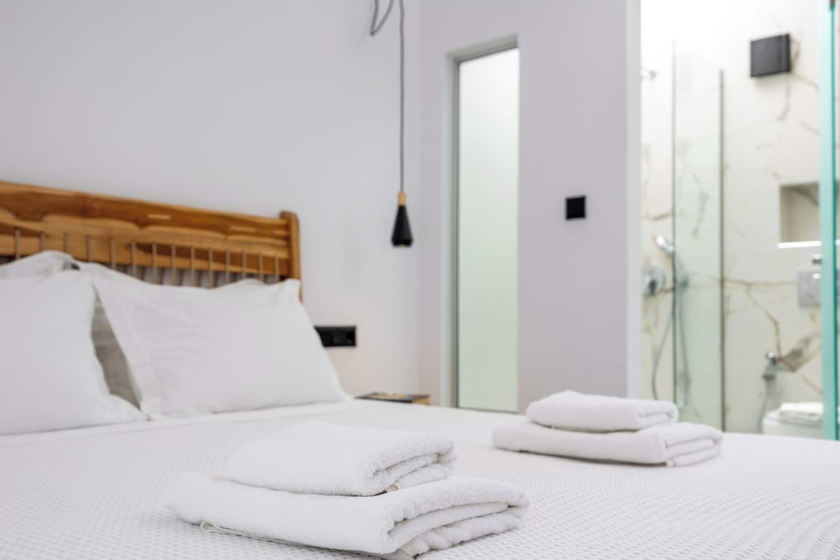 A neatly made bed with white linens, a wooden headboard, and a hanging light fixture.