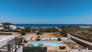 A pool area with lounge chairs and umbrellas, a clear view of the sea, and a white building with a balcony. - Delight Apartments Suites (Naxos)