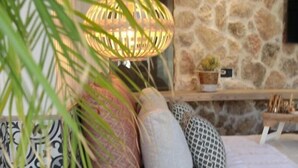 A cozy bedroom with a stone wall, a bed with patterned pillows, a bedside table, and a hanging lamp. - Delight Apartments Suites (Naxos)