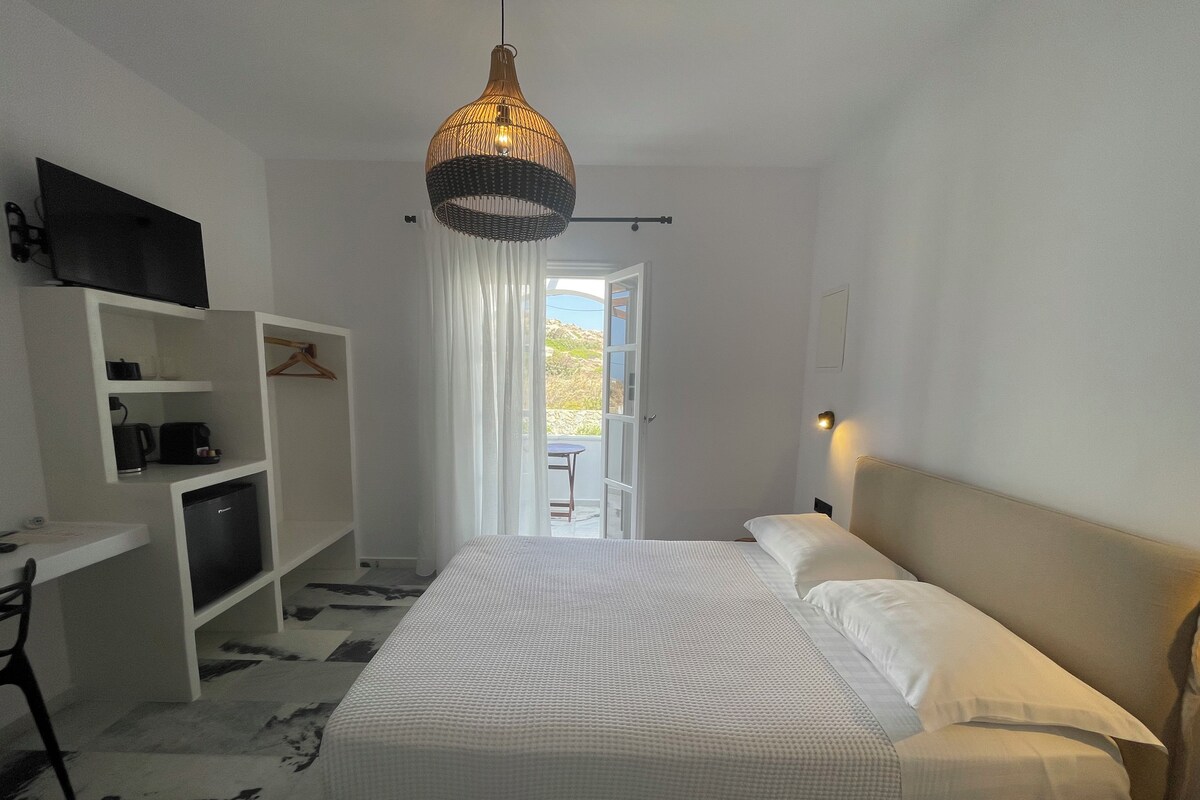 A hotel room with a bed, a desk with a TV, a wardrobe, and a balcony with a view.