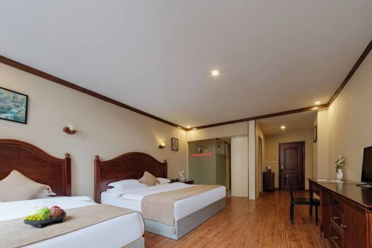 A hotel room with two beds, a desk, a chair, and a television.